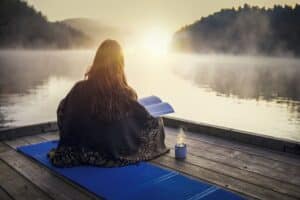 Young woman sitting on a pier and relaxing with book and coffee on sunrise.